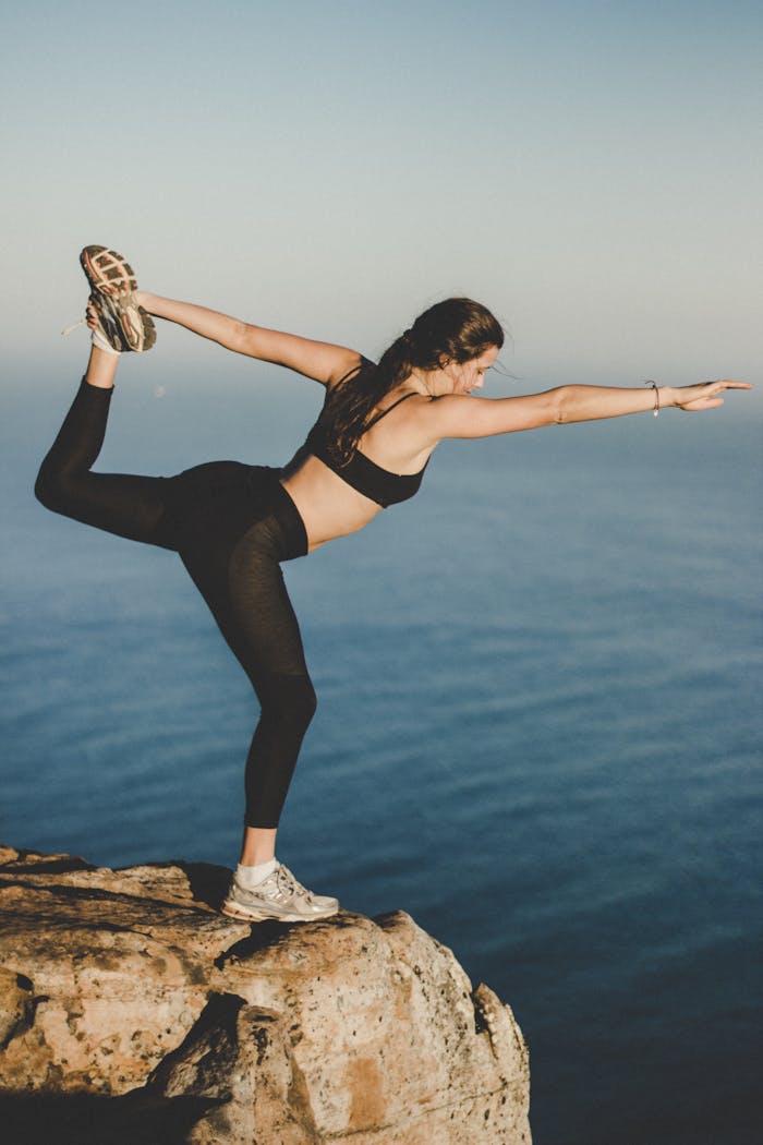contact-bg Woman practicing yoga in Dancers pose on a cliff with ocean view, Cape Town.
