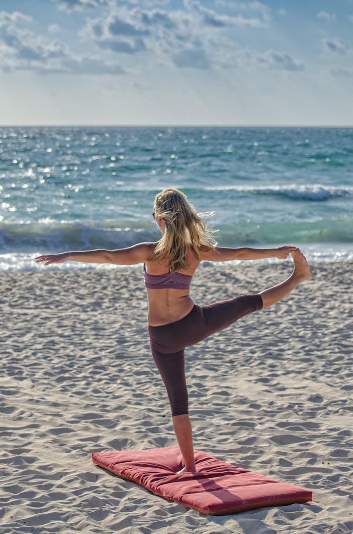 team-04 A woman performs yoga on a sandy beach at sunrise, embracing wellness and tranquility.