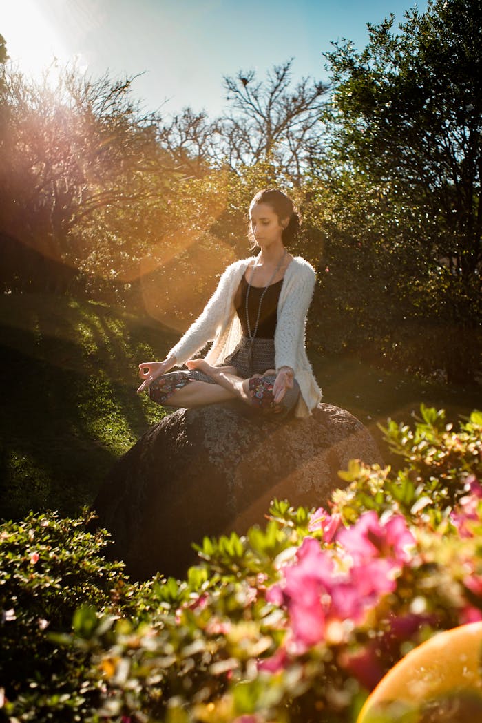 team-05 Woman in tranquil meditation pose outdoors, bathed in sunlight, surrounded by lush greenery.